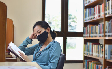 Woman with protective mask reading a book in library