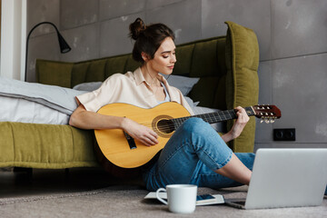 Image of young caucasian brunette woman playing acoustic guitar at home