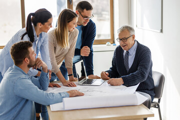 College professor examining blueprint with group of his students.	
