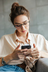 Image of thinking woman using mobile phone while sitting on couch