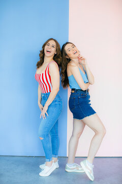 Photo of emotional two women friends standing isolated over color background. Looking camera showing peace and rock gesture.