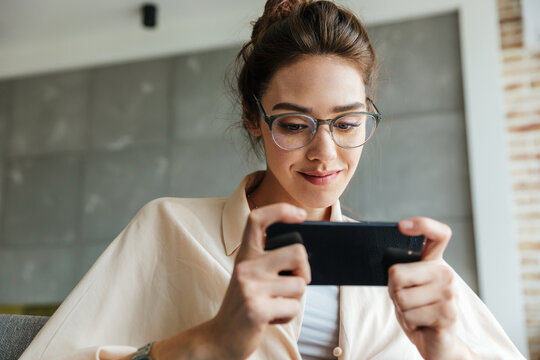 Image of smiling attractive woman playing video game on mobile phone