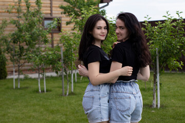 Two young brunette women in a black T-shirt and denim shorts hugging. Sisters, girlfriends. family and friendship concept. High quality photo