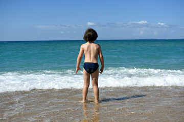 Fototapeta na wymiar Little boy enjoying on beach. Child sit on beach and play in sea on summer vacation