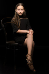 Fototapeta na wymiar Portrait of a little girl sitting on an old Viennese chair, black background.