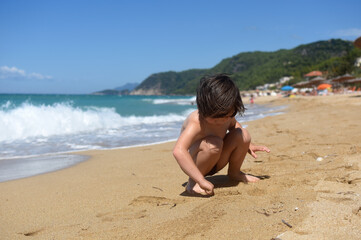 Fototapeta na wymiar Child playing in sand on the beach. Cheerful boy play on send on summer holiday