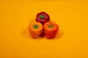 Sweet peppers yellow, orange, red on a yellow background, top view