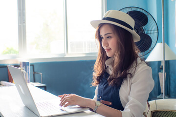 Young smiling business asian entreprenure woman using smartphone with computer in home office