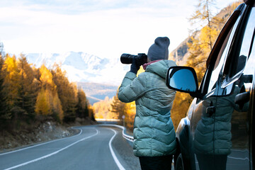  Woman traveler taking a photo on mountain with car on roadtrip, autumn vacation. beautiful hipster...