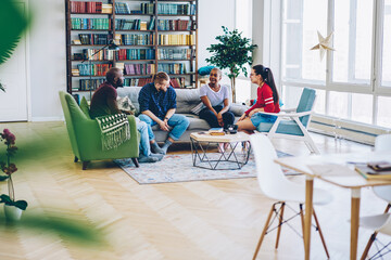 Multiracial group of hipsters sitting on comfortable couch in contemporary apartment communicating,...