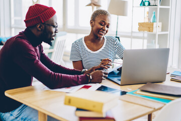 Young african american colleagues discussing ideas for project using laptop computer for work, skilled dark skinned male and female students cooperating on project communicating sitting at desktop.