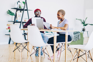 Young african american couple checking bills and receipts for paying online via application on laptop computer, dark skinned colleagues discussing ideas and making plans using modern technology