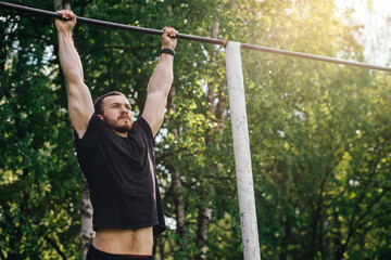 Muscular athlete man making Pull-up in gym outdoors on summer da