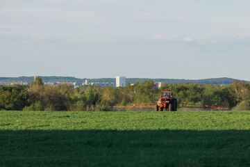 Obraz premium Tractor spraying pesticides on field with sprayer at spring