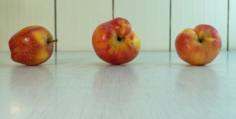 Three deformed red and yellow apples on rustic table in the kitchen. Organic fruits good for diet, because contain a lot of vitamins and microelements. Horizontal orientation image with copy space.