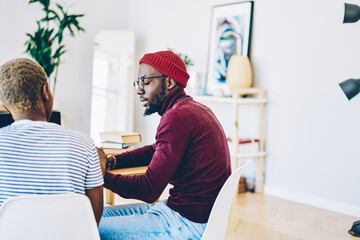 Cropped image of serious dark skinned hipster guy explaining smth to his female colleague, african...