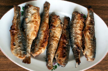 Fried fish in a white plate on a wooden table