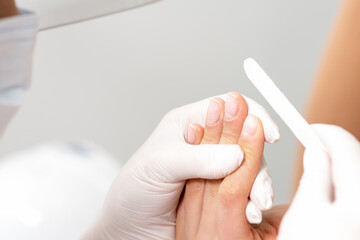 Close up of hands of manicure master doing manicure procedure by nail file.