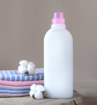 One bottle of white fabric softener and stack of towels with cotton flowers on a wooden table. Laundry day. Mockup