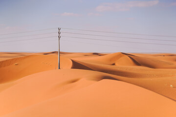 gorgeous desert of reddish sand dunes with power lines and utility poles on the horizon