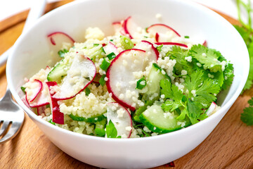 Fresh summer vegetable salad of couscous, radish, cucumbers, parsley and lemon. Vegan food. Spring or summer food. Salad with couscous and raw vegetables close-up.