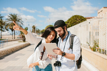 Couple looking at a tablet in the middle of the street while she is pointing to one direction