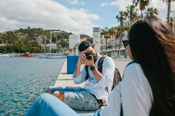 Man taking a photo with a camera of a girl sitting in front of the sea