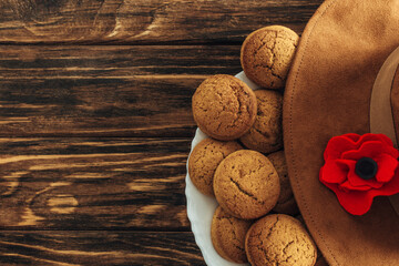 top view of artificial flower, felt hat and cookies on wooden surface, anzac day concept