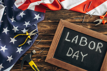 top view of american flag, metallic nails and instruments near chalkboard with labor day lettering on wooden surface