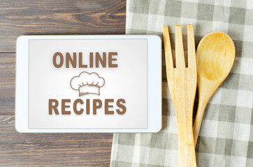 Online recipes. Cookbook in a tablet computer. Kitchen utensils. Brown wooden background