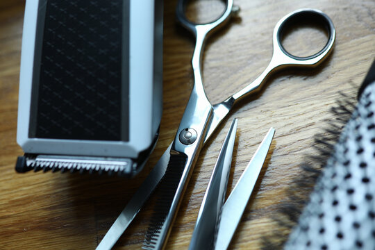 Close-up Of Scissors For Cutting And Thinning Out Clients Hair. Electrical Clippers. Professional Hairdresser Equipment For Work In Salon. Metal Instruments Laying On Wooden Desk