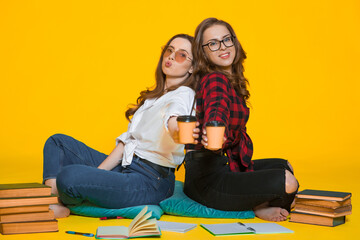 Photo of a cheery laughing young girls student friends sitting on yellow background drinking coffee talking with each other.