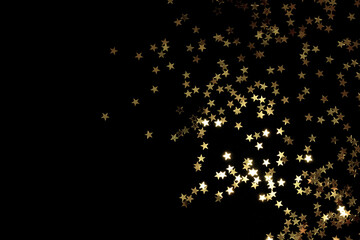 Golden stars confetti scattered on a black background. Creative holiday concept.