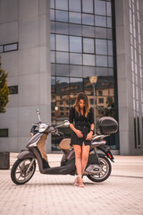 Fototapeta na wymiar Lifestyle session on a motorcycle, a young blonde Caucasian businesswoman with a black blazer and white pants. Perched next to a motorcycle in the city