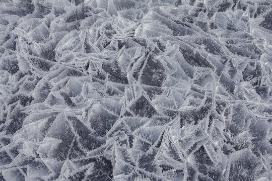 Danger on the show surface: cracks in blue ice of cracked glacier in textured white snow surface under sunlight, closeup view, winter