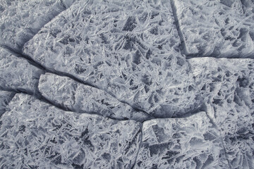 Danger on the show surface: cracks in blue ice of cracked glacier in textured white snow surface under sunlight, closeup view, winter