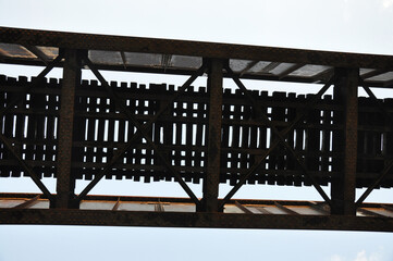 suspended railroad tracks running across a bridge as seen from underneath with sky visible between slats