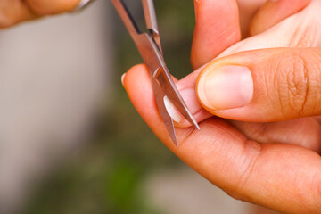 Mother hold childs finger and cut fingernail by nail scissors.