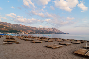 A deserted sand beach in Montenegro. Closed beach umbrellas and orange deck chairs against the backdrop of the Adriatic Sea.
