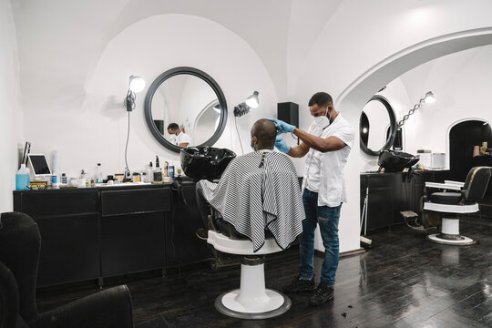 Barber wearing surgical mask and gloves cutting hair of customer