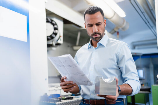 Businessman holding plan and workpiece in factory hall