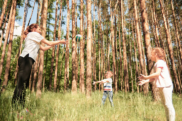 a mother and two small children play with a ball in a beautiful pine forest. 