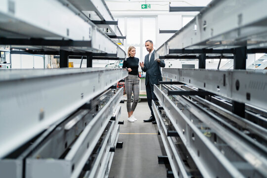 Businessman and woman at metal rods in factory hall