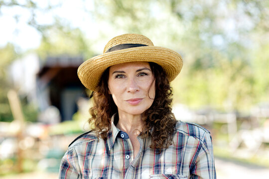 Portrait of confident mature woman wearing sun hat standing at community garden
