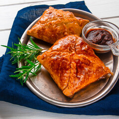 Homemade pastries with meat and spicy sauce with rosemary served on a metal tray on white wooden table