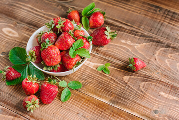 Ripe sweet strawberries in white plate on the wooden background. Copy space