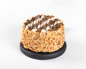 Biscuit cake with cream, caramel, nuts and chocolate on a light background 