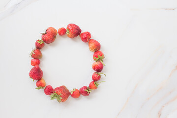 Obraz premium Round frame of ripe fresh strawberries on white marble with copy space. Summer and fruit concept, top view, flatlay