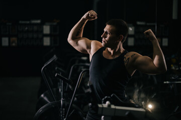 Fototapeta na wymiar Muscular strong man with perfect beautiful body wearing sportswear standing in pose Champion in dark modern gym. Concept of healthy lifestyle.
