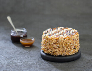 Biscuit cake with cream, caramel, nuts and chocolate on a dark gray background 